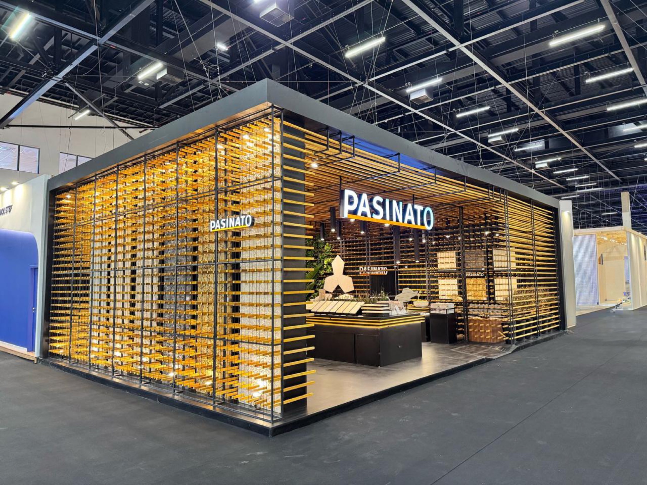 Stand da Pasinato na Expo Revestir, com fachada preta e ripas douradas iluminadas